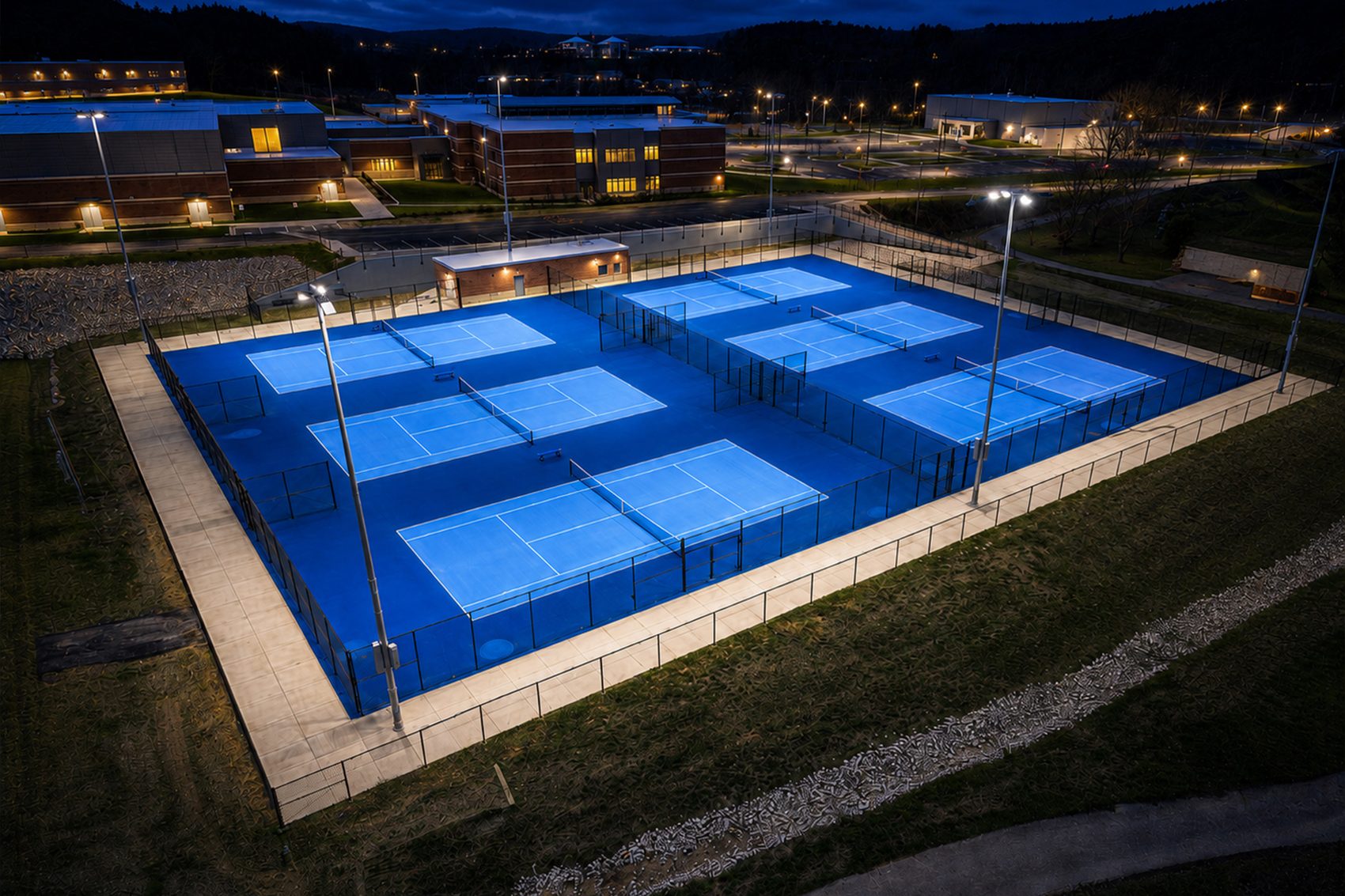 The lit tennis courts at dusk, with the campus glowing in the background