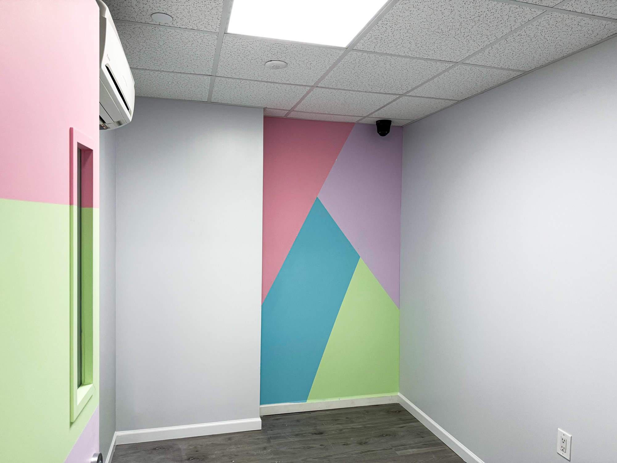 Playroom accent wall with a bright geometric mural in pink, teal, green and lilac
